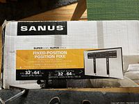 Photo showing Sanus branding and product details including size range 32-64 inches and weight holding capacity of 150 lbs.