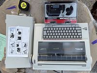 Top view of Smith Corona DLX 100 electric typewriter with an extra ribbon cartridge in its package placed on top.