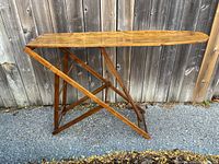 Side profile showing the ironing board's foldable wooden X-frame legs and rectangular top