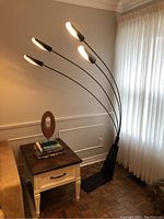 Full view of black metal arc floor lamp with five lit heads next to side table