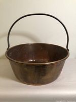 Front view of vintage brass pot with iron handle, showing patina and round shape.
