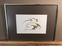 Full view of framed ink and watercolour artwork by Eddy Cobiness depicting stylized birds in black and gold tones on white paper with dark mat and metal frame.