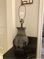 Front view of the lamp showing the embossed decorative metal body, dark patina finish, bulb socket, and cord.