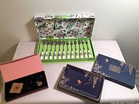 Full lot display: boxed set of Portmeirion pastry forks and spoons with floral patterned handles, blue floral and bird design Portmeirion serving dish, and Holt Renfrew enamel purse holder with matching mirror and charm pieces in black presentation box.