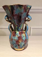 Multicolored ceramic vase showing front view with flared scalloped rim and double curved handles with gold accents