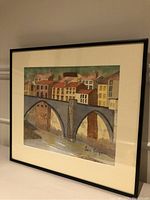 Framed watercolour landscape painting by John Bergman featuring a stone arch bridge and buildings, showing entire piece and frame.