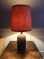 Table lamp lit, showing red-orange textured shade and distressed copper base with blue glass accents.
