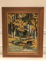 Full view of framed painting showing a deer in a woodland scene with trees and a stream.