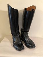 Front view of the pair of black leather riding boots showing tall shaft and smooth leather with wear marks.