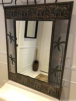 Front view of rectangular mirror with stamped faux copper frame adorned with elephant and palm tree motifs.