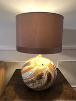 Side view of the round ceramic table lamp with faux marble glaze and brown fabric lampshade, lamp turned off.