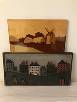 Front view of two wood marquetry art panels showing a windmill scene on top and a village street scene on bottom.