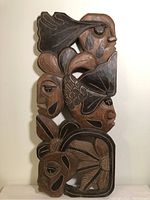 Front view of the full cedar carving showing multiple stylized faces, leaves, and fish in dark and natural wood tones.