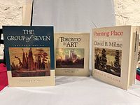 Three Canadian art coffee table books displayed upright: The Group of Seven by Charles Hill, Toronto in Art by Edith G. Firth, Painting Place by David Silcox