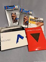 Top-down view of six different packets of new ladies stockings on a gray surface. Brands visible include WonderBra, Sanpellegrino, Sigvaris, and Dolci Calze. Packaging states new and some show images of legs wearing the stockings.