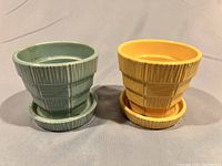 Front view of turquoise and yellow McCoy pots with attached saucers on neutral background.