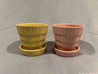 Two McCoy pottery pots with attached saucers, one pink and one yellow, shown side-by-side front on