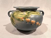 Side view showing blue glazed jardiniere with raised relief of green leaves and orange bleeding hearts flowers.