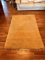 Full view of the yellow cotton rug placed on wooden floor, showing the rectangular shape and fringed edges on shorter sides.