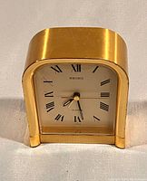 Front view of vintage Seiko quartz clock with Roman numeral face and brushed brass case.