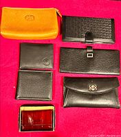Set of seven leather wallets and key holder displayed on red surface showing various styles, colors, and sizes.