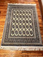 Full view of the rectangular wool rug laid flat on hardwood floor showing overall pattern and fringes at ends.