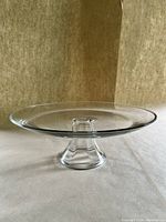 Clear glass cake stand with bevelled base photographed against neutral background to show full profile and details of shape and rim.