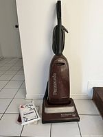 Front view of Panasonic upright vacuum cleaner standing upright with package of vacuum bags placed beside it on floor.