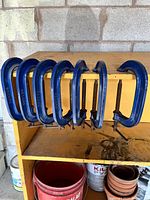 Seven blue metal C-clamps arranged on a shelf.