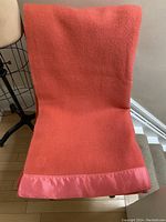 Coral wool blanket draped over chair showing color and satin binding edge.