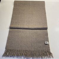 Full view of folded pale tea colored alpaca scarf showing overall texture and fringed end.