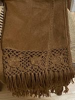 Close-up of one end showing the hand-crocheted floral lacy pattern and 4-inch fringe in cinnamon alpaca wool