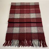 Folded view of burgundy, grey, cream, and black checkered cashmere scarf with fringed ends.