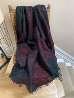 Mohair blanket draped over a wooden chair showing burgundy and dark blue checks with fringed ends.