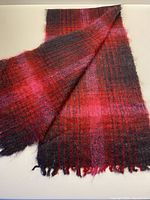 Full view of the mohair scarf showing its red and purple checkered pattern with fringed ends on a flat surface.