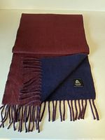 Wool scarf folded to show cherry red side and partially lifted dark blue reverse side with fringed ends.
