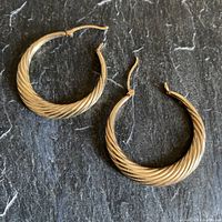 Pair of gold hoop earrings displayed on dark textured surface.