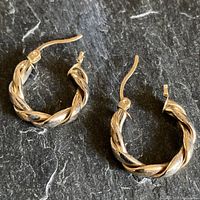 Pair of yellow 10K gold twisted textured hoop earrings on dark surface, showing full view with closures.