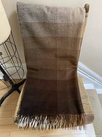 Photo showing the full blanket draped over a chair, displaying the gradient squares in shades of brown and fringed tassels.