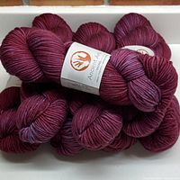 Eight skeins of deep cherry maroon yarn balls stacked together with labels visible.