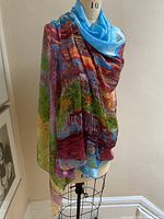 Front view of scarf draped on dress form showing flowing fabric and vivid color pattern in blue, red, green, purple, and orange tones.