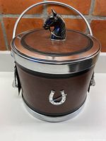 Front view of the ice bucket showing brown vinyl covering, silver horseshoe on front, metal rim, and carrying handle.