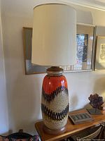 Full view of tall ceramic lamp with orange, cream, and dark brown glaze and teak base under natural light