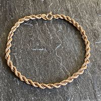 Full view of twisted rope chain bracelet on dark surface showing overall shape and clasp