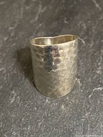 Front angled photo of chunky sterling silver ring with visible hand hammered texture on black surface.