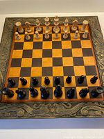 Full view of chessboard set up with all wooden pieces in starting position. Board has decorative metal border and walnut trim, 8x8 alternating squares in wood.