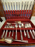 Full set of Oneida Coronation cutlery arranged in a red velvet box showing the various knives, forks, spoons and serving pieces with detailed handles