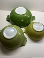 Underside of three Pyrex Cinderella bowls inverted to show white base and colored exterior shades of avocado green