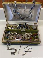 Jewelry box open showing various silver chains hanging inside the lid and a mix of necklaces and costume jewelry inside the compartments.