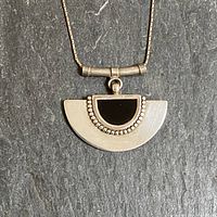 Close up of the sterling silver half-moon pendant with black onyx inset and surrounding silver spheres on dark slate surface.